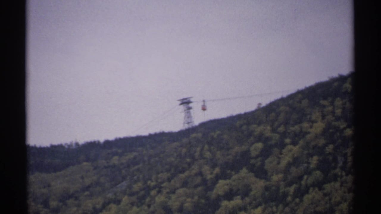 Cable car suspended near a support tower over wooded hills.