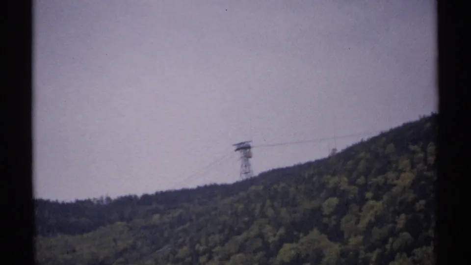 End frame of a 1971 New Hampshire mountain tramway scene, with the tower and suspended car seen across dense forest.