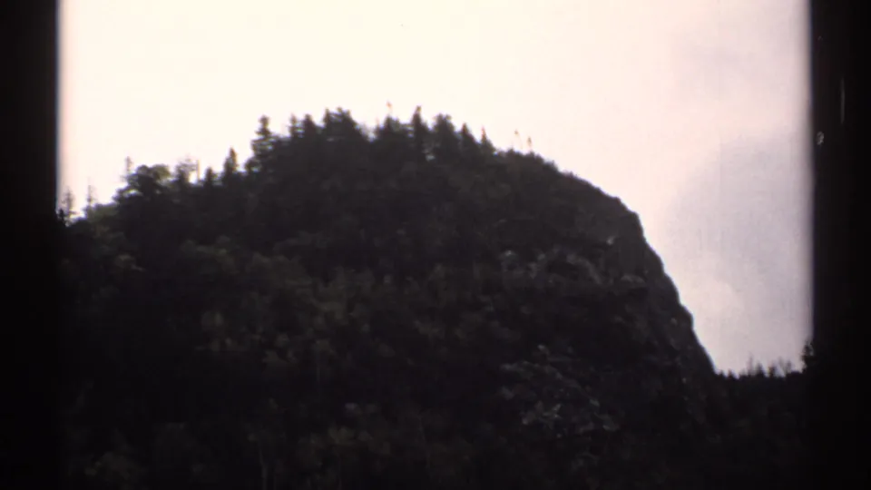 The view shifts to a tree-topped rocky mountain face, consistent with the New Hampshire tramway setting.