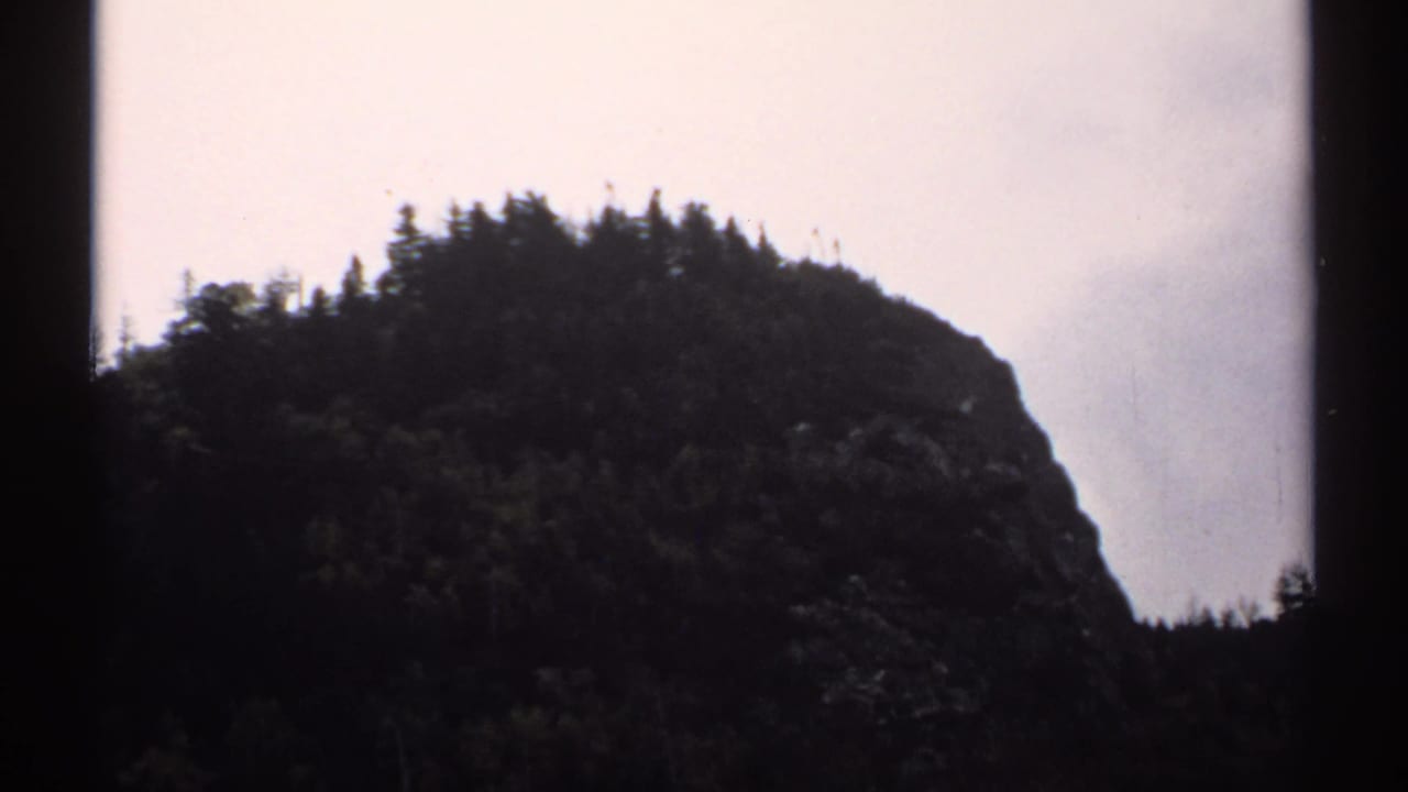 Dark forested mountain slope silhouetted against a pale cloudy sky.