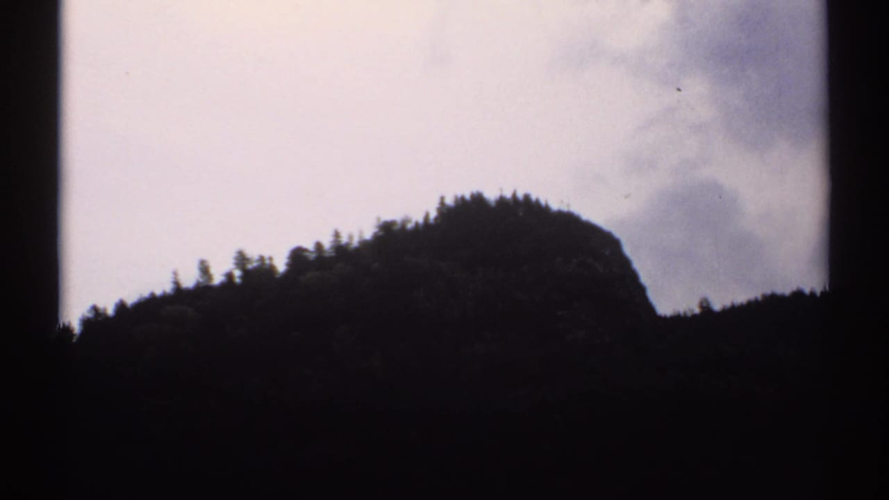 Rounded wooded mountain peak seen in silhouette below a cloudy sky.