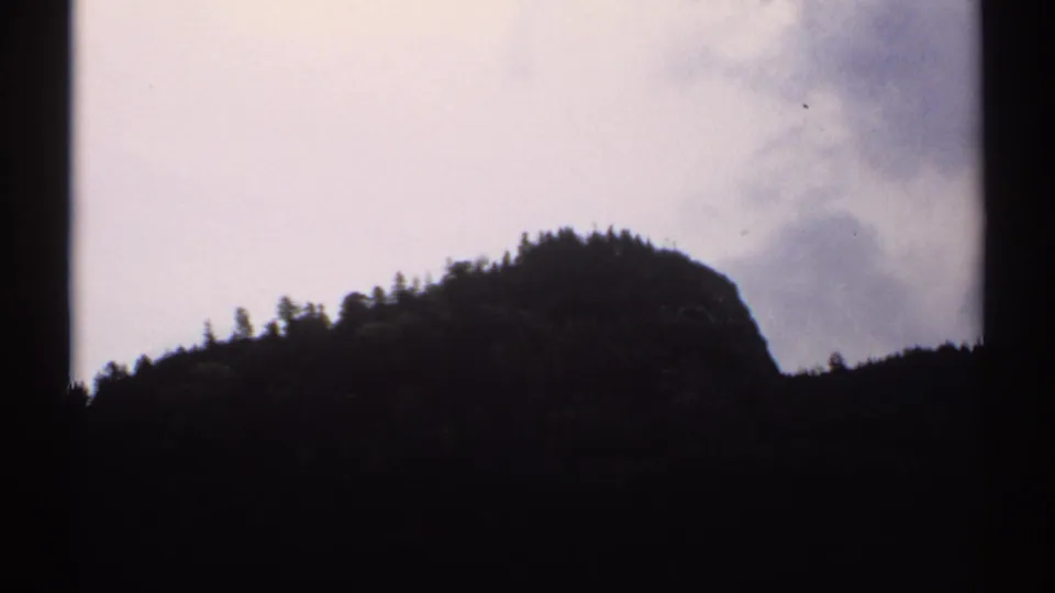 1971 New Hampshire 8mm view of a rounded, wooded peak silhouetted against pale cloud cover.