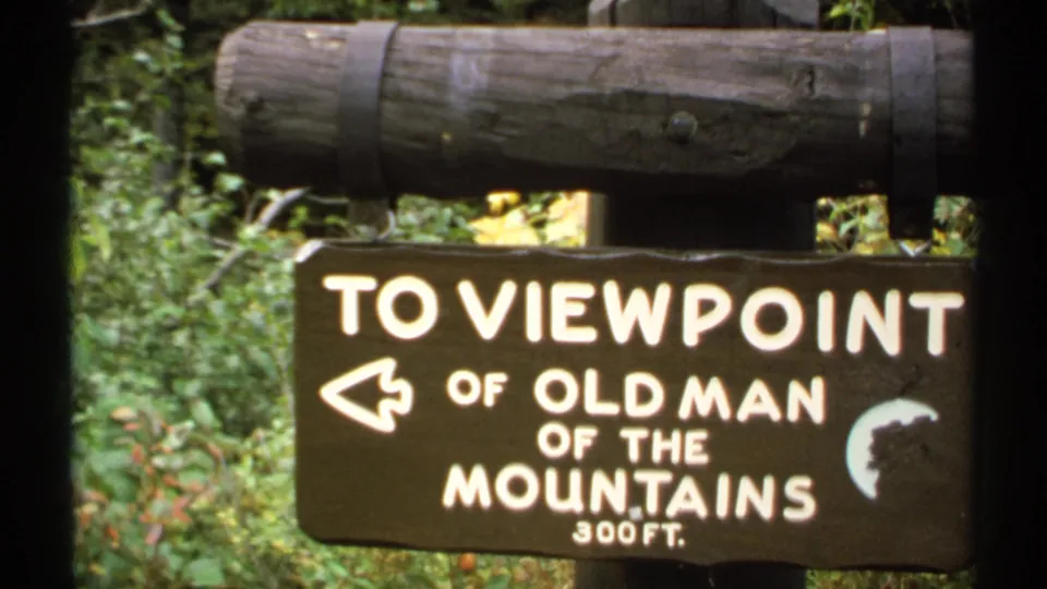 1971 home-movie frame of a rustic New Hampshire sign pointing toward the Old Man of the Mountains viewpoint.