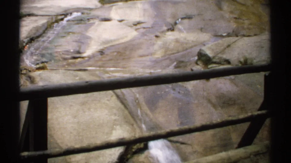 Close view of a rocky forest stream in New Hampshire, with water moving through cracks in the stone behind metal railings.