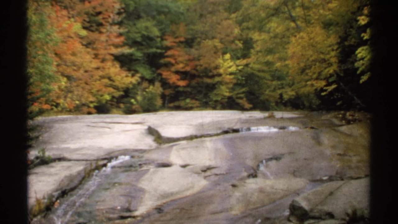 Rock ledges with thin streams of water below colorful autumn woods.