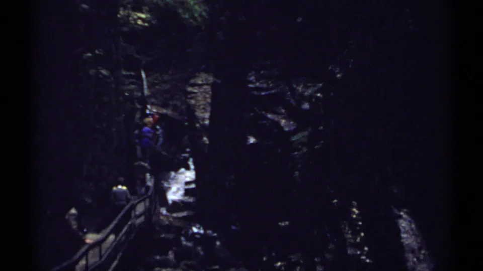 1971 New Hampshire 8mm frame showing visitors along a railed walkway in a rocky gorge with bright water below.