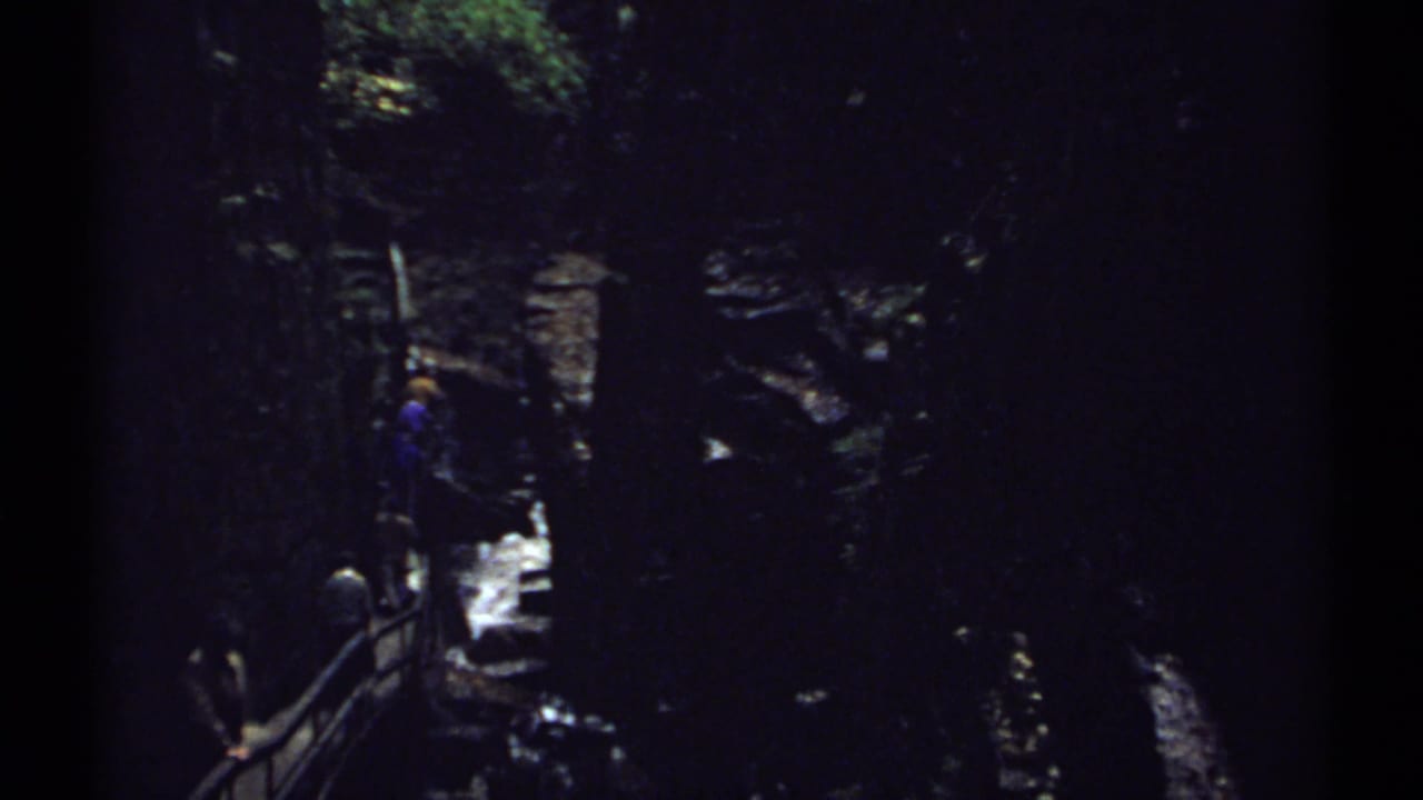 Dark ravine trail with visitors near railings and bright water below.