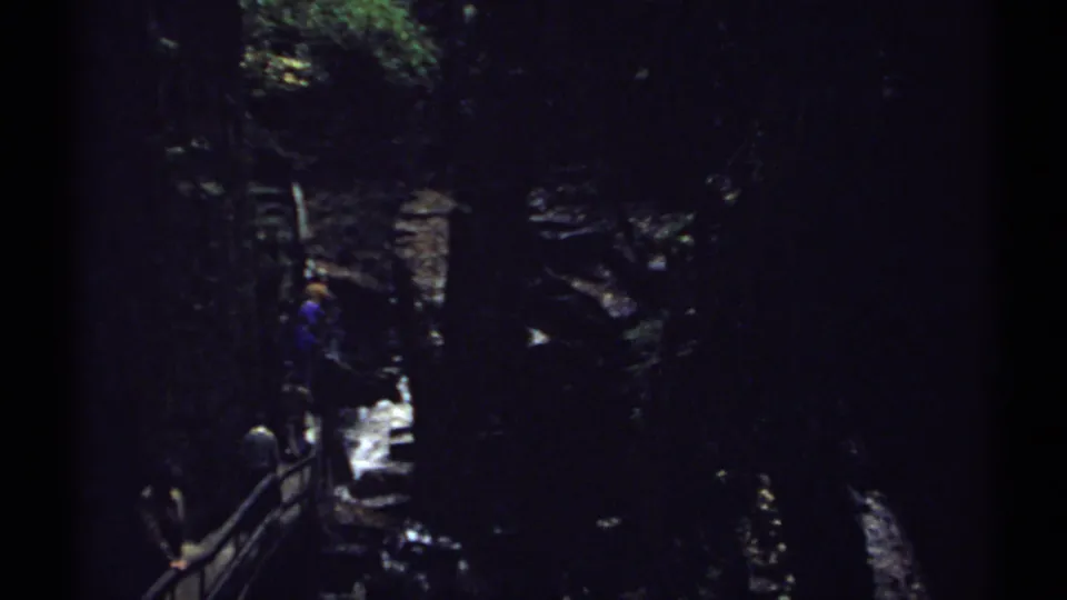 1971 New Hampshire 8mm frame showing visitors on a shaded ravine stairway near white water and rock walls.