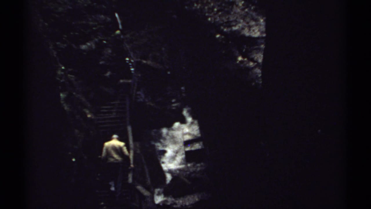 Man in a light jacket climbs a narrow staircase in a dark ravine.