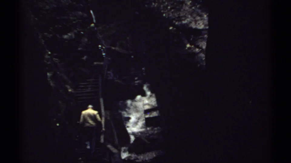 A man in a light jacket ascends metal stairs through a shaded New Hampshire ravine, with white water visible below.