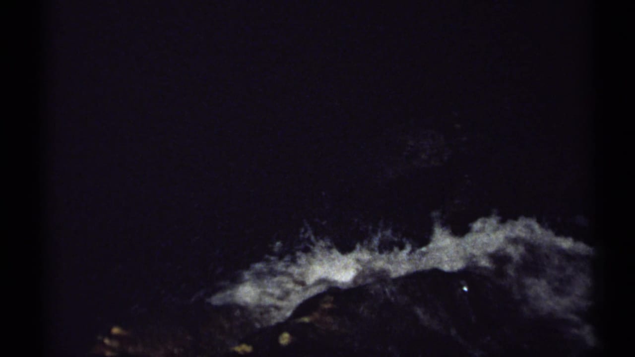 Dark frame with white water rushing over rocks near a shadowed waterfall edge.