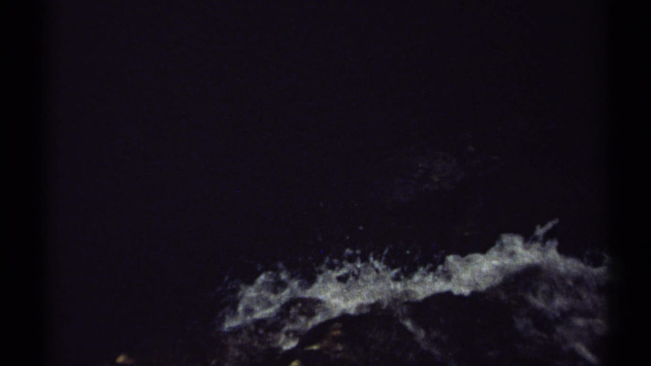 White water splashes across a dark rocky surface in a shadowed waterfall view.