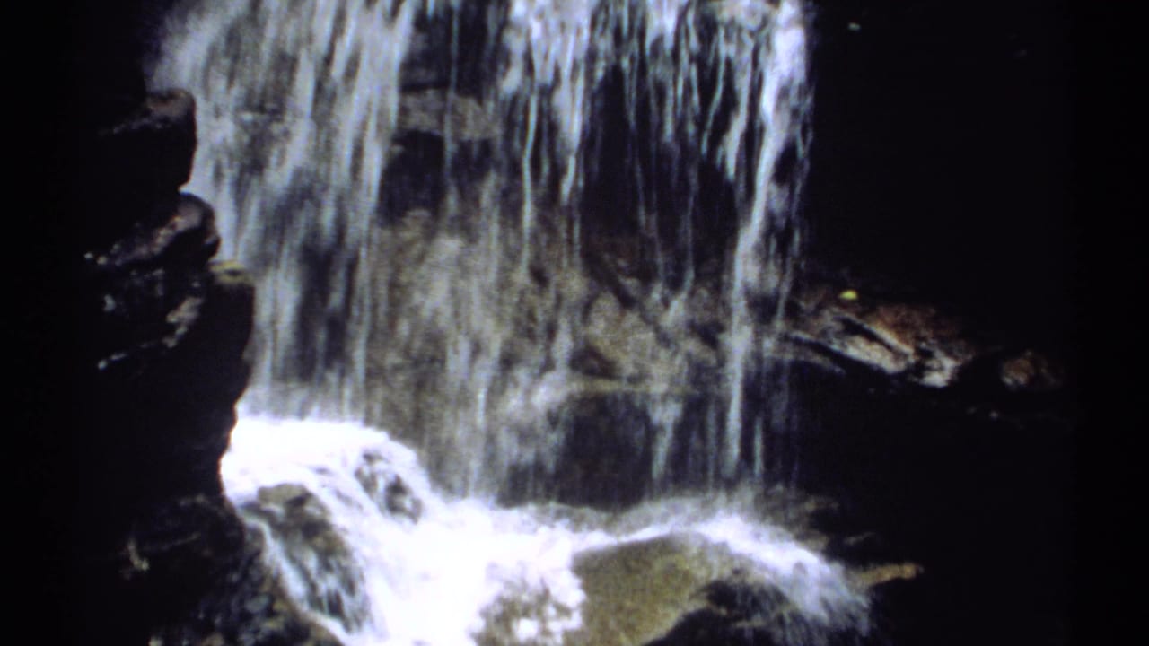 Waterfall dropping over dark rocks with white froth and deep shadow.