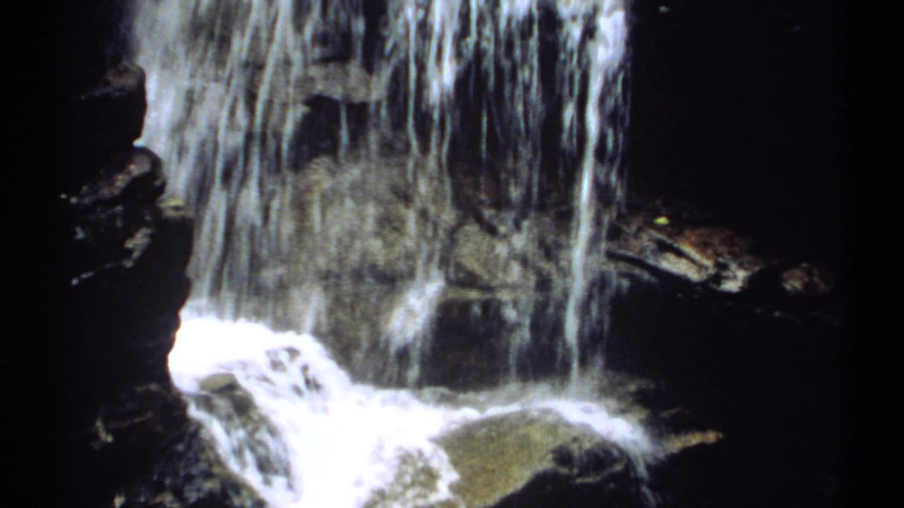 Close waterfall view with bright flowing water across dark stone.