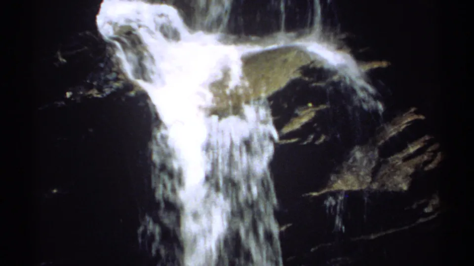 1971 New Hampshire 8mm frame showing the lower section of a waterfall pouring through dark rocks with foamy highlights.