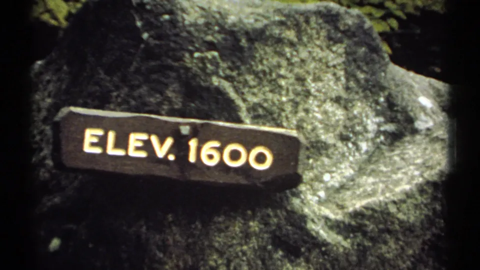 Close view of a wooden ELEV. 1600 marker attached to a boulder in 1971 New Hampshire home-movie footage.