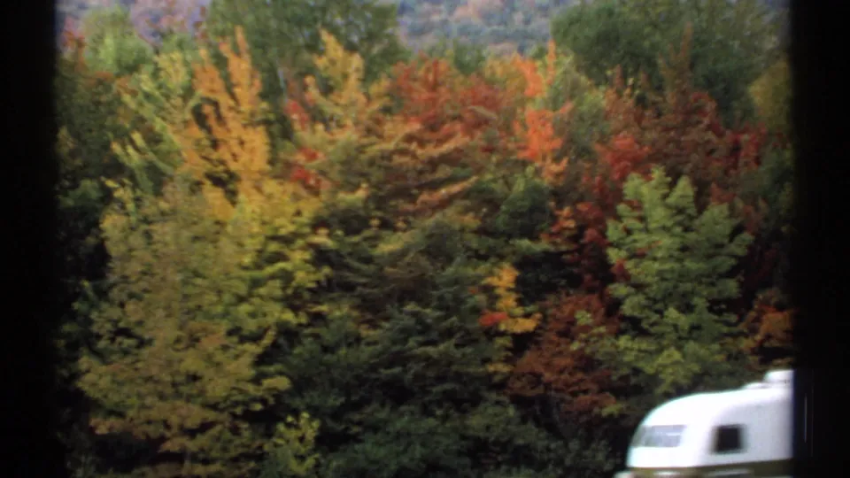 A silver travel trailer passes below dense New Hampshire autumn foliage in a 1971 home-movie frame.