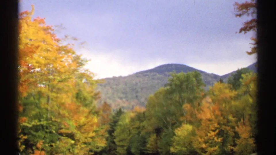1971 New Hampshire home-movie view of bright autumn foliage with a rounded mountain beneath a pale cloudy sky.