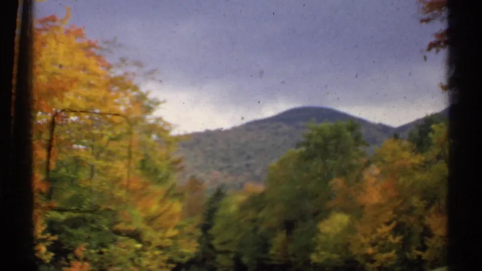 1971 New Hampshire frame showing a rounded mountain beyond red, yellow, and green autumn trees in a soft home-movie scan.