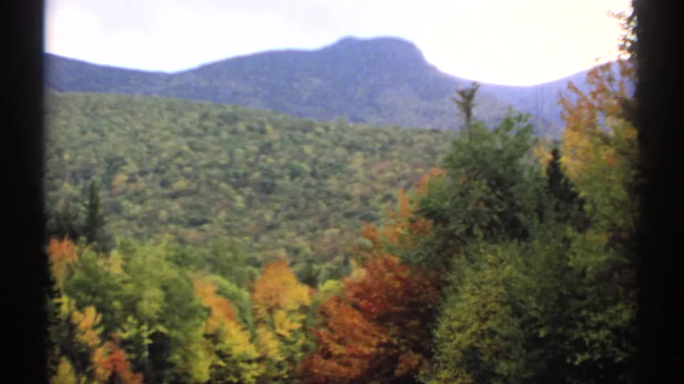 1971 New Hampshire 8mm landscape of a forested valley, autumn-colored trees, and a rounded blue-gray mountain ridge.