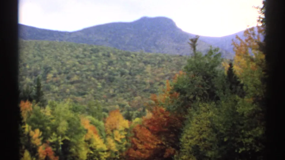 New Hampshire autumn landscape on 8mm film, showing a mountain beyond dense forest in mixed green, red, and gold foliage.