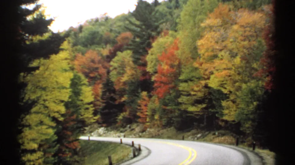 1971 New Hampshire 8mm roadside view of a winding two-lane highway bordered by colorful fall trees and evergreens.