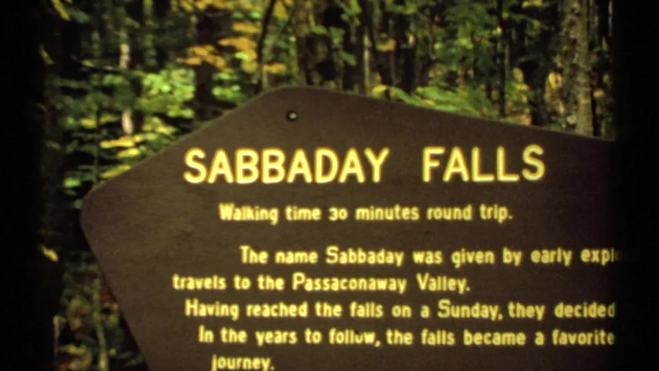 1971 New Hampshire 8mm frame showing a wooden Sabbaday Falls sign among trees, with text about a 30-minute round-trip walk.