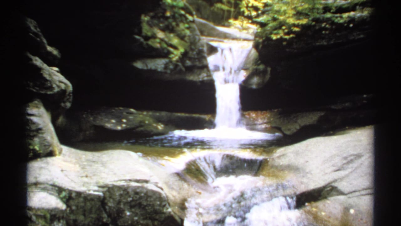 Small waterfall dropping between layered rocks into a shallow pool.
