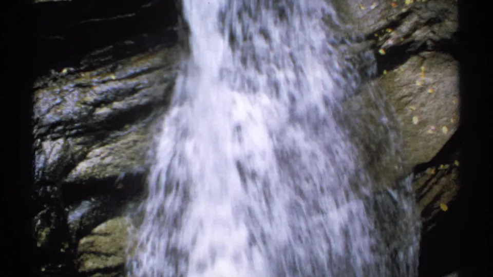 1971 New Hampshire 8mm frame showing foamy white water descending over stacked dark rocks with a close home-movie view.