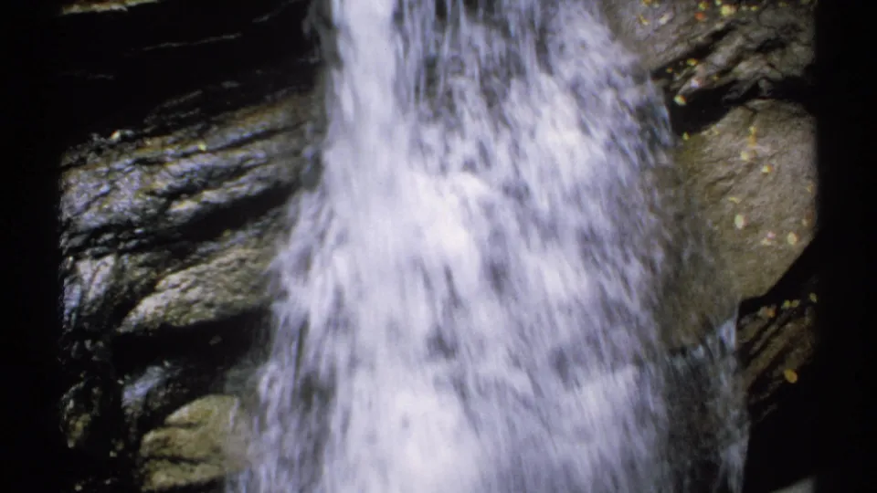 1971 New Hampshire 8mm frame of white water splashing beside rounded wet rock and dark ledges in a tight natural close-up.