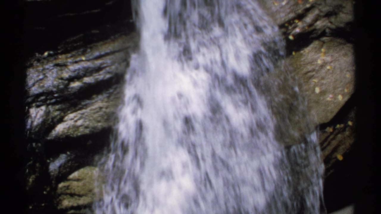 1971 New Hampshire 8mm frame showing bright falling water against dark layered rock.