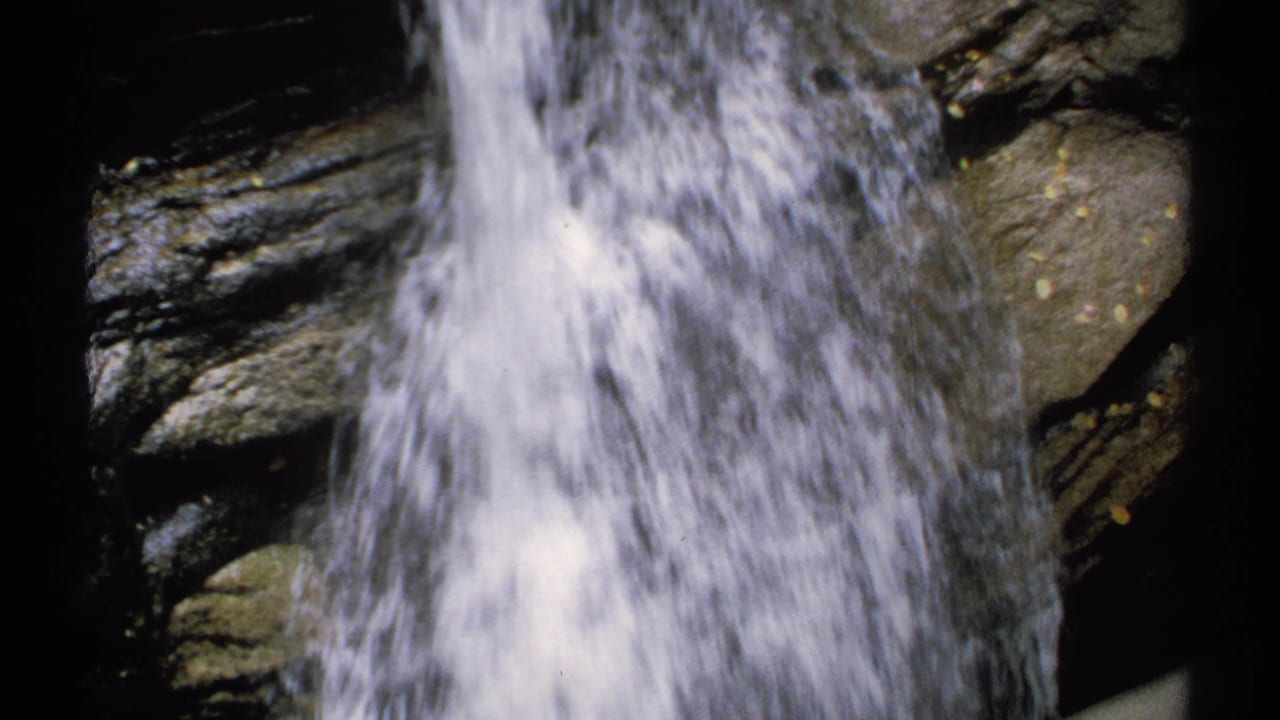 Waterfall stream falling beside dark rocky ledges.