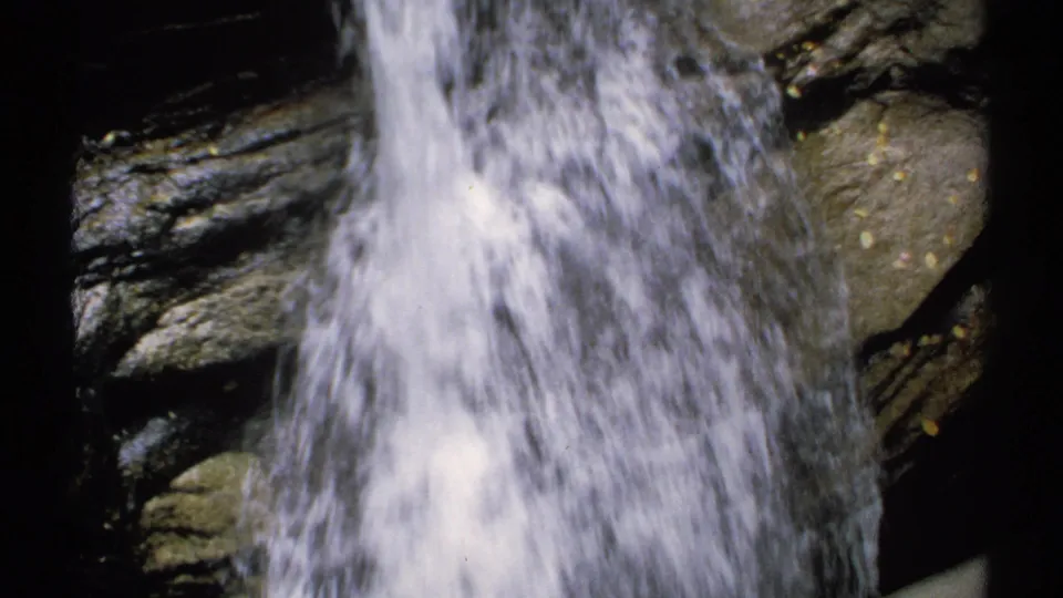 Close 8mm view of a New Hampshire waterfall, with white water moving past dark stone.