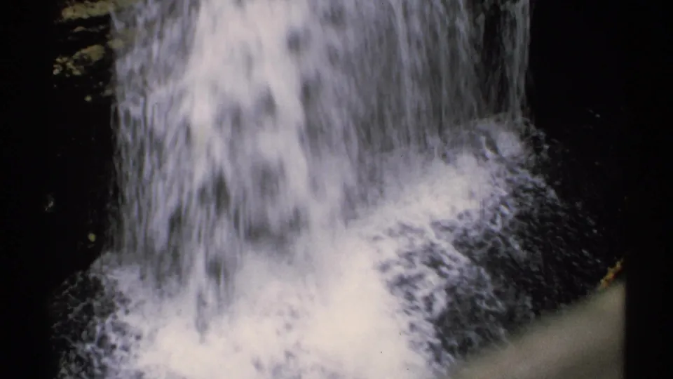 Vintage 8mm frame of a New Hampshire cascade dropping into frothy water amid shadowed rocks.