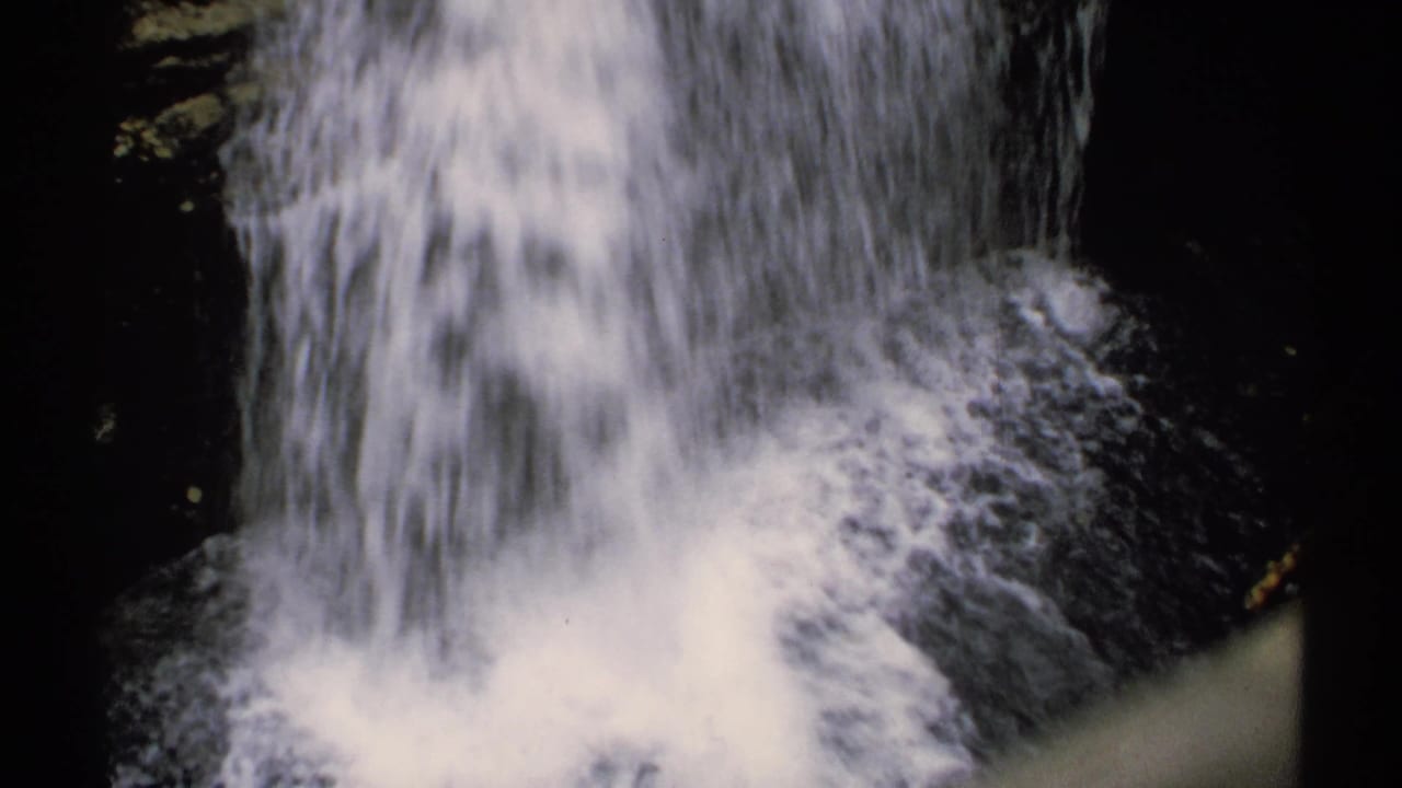 White waterfall rushing over dark rocks in a wooded setting.