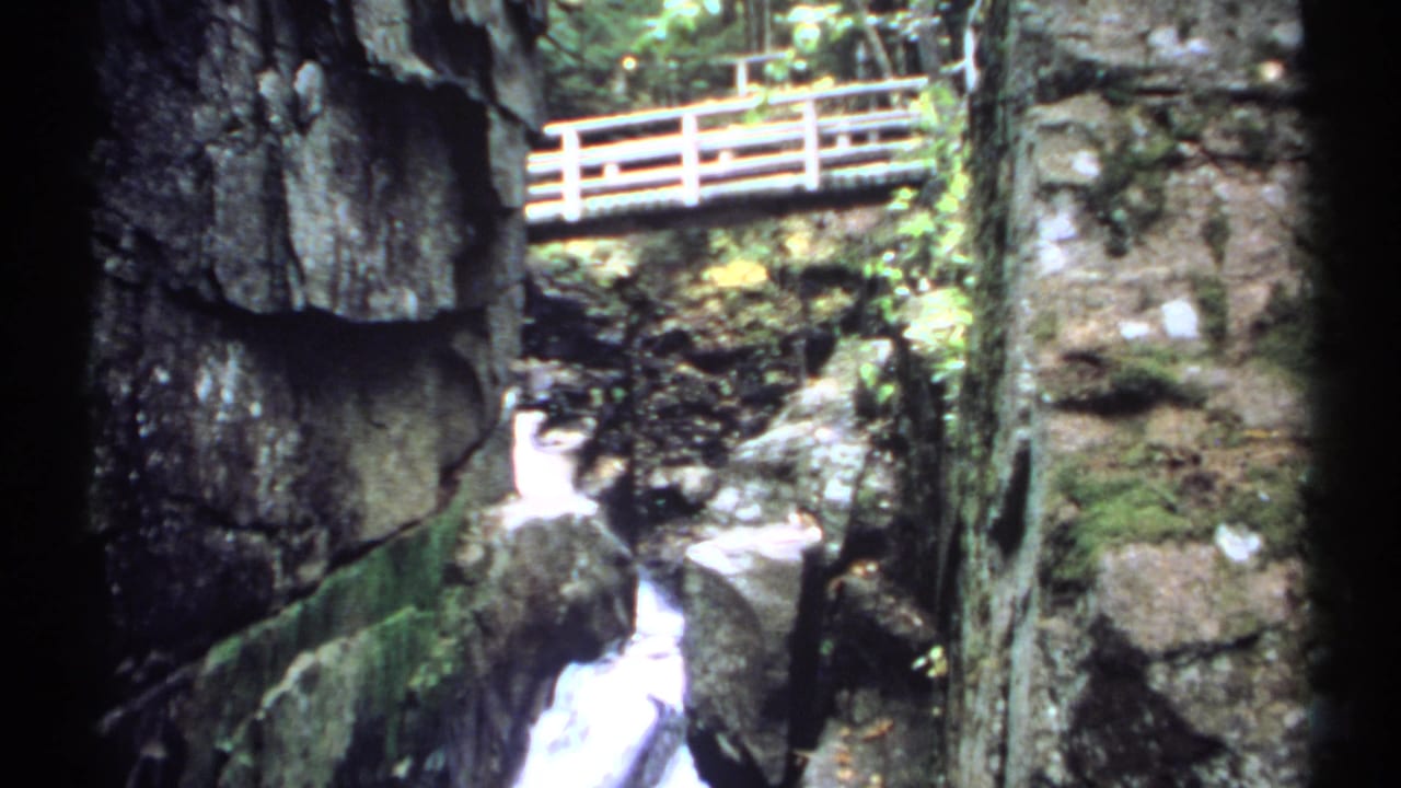 Wooden bridge above a narrow waterfall in a rocky gorge.