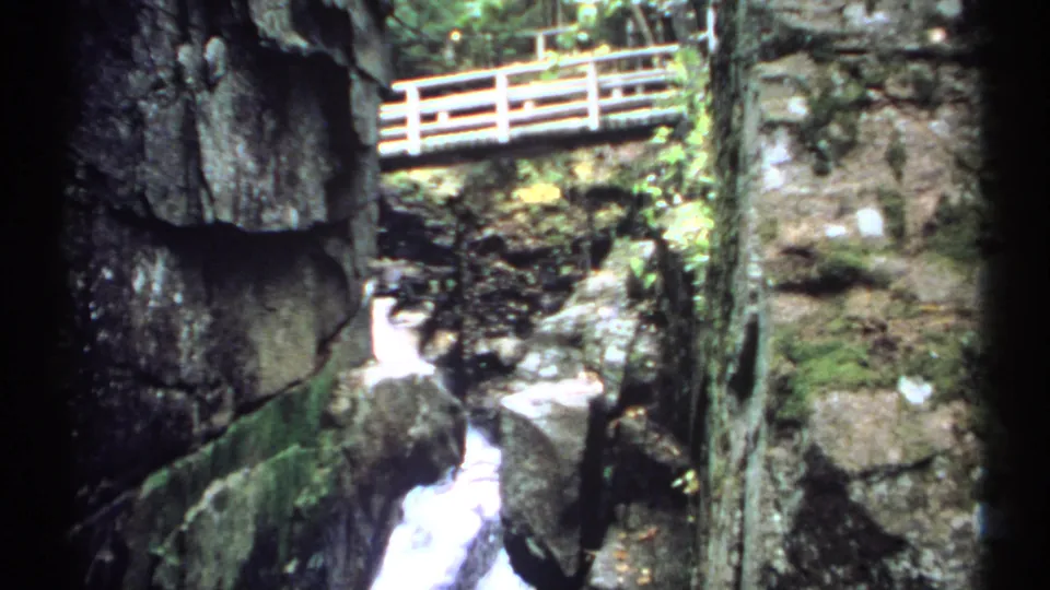 1971 New Hampshire 8mm frame showing a close view of the gorge wall, white water, and bridge railing above.