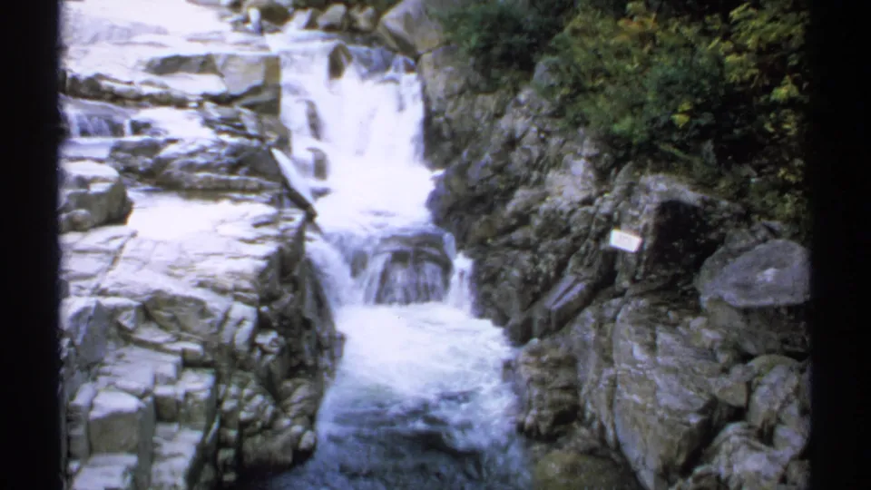 1971 New Hampshire 8mm frame showing a closer waterfall view, with white water flowing over dark rocks into a narrow stream below.