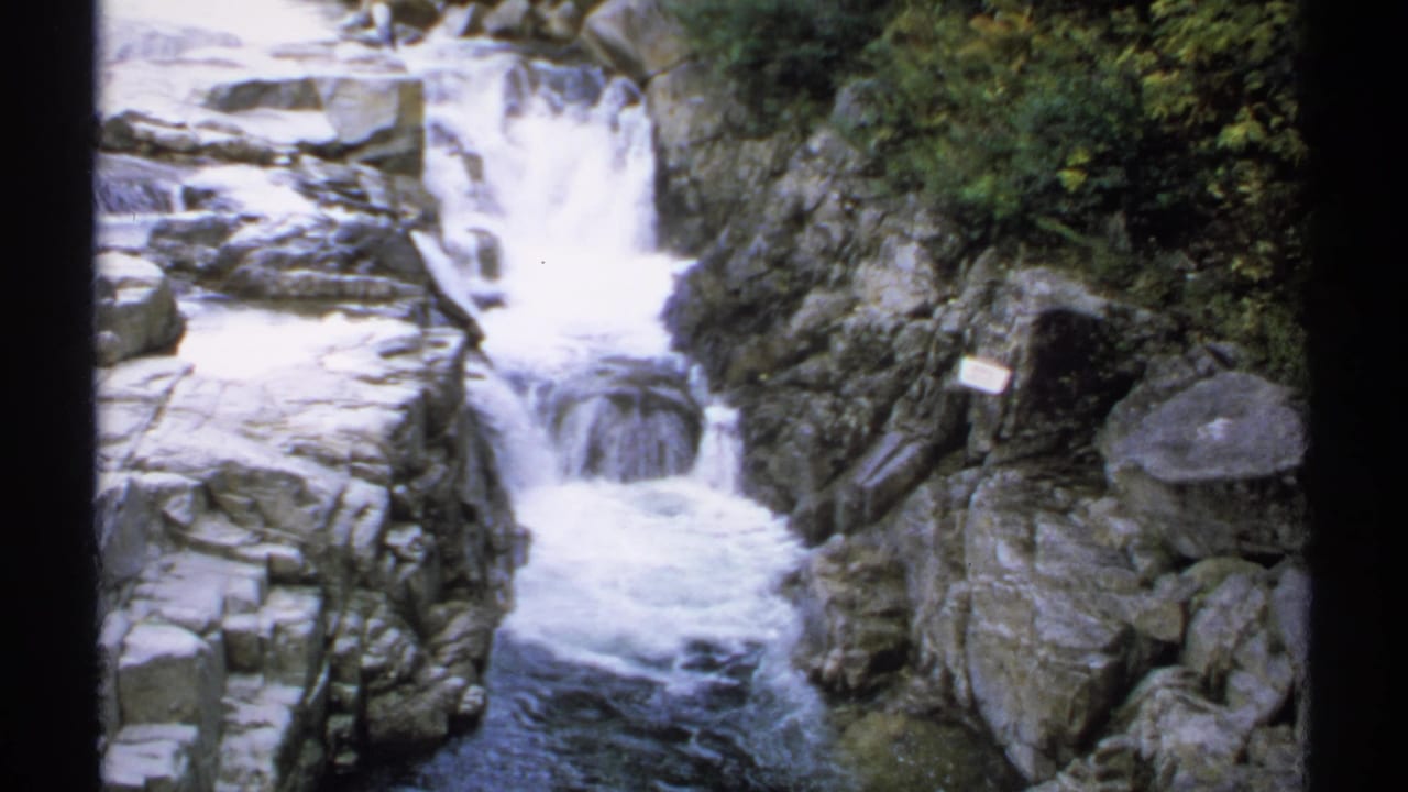 Waterfall cascading over gray rocks with forest foliage around the gorge.