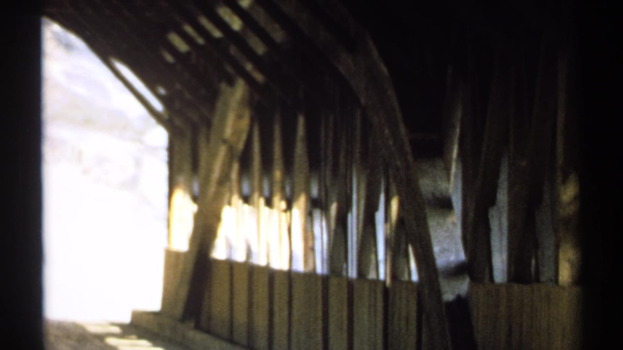 Dim covered bridge interior with bright side opening and wooden beams.