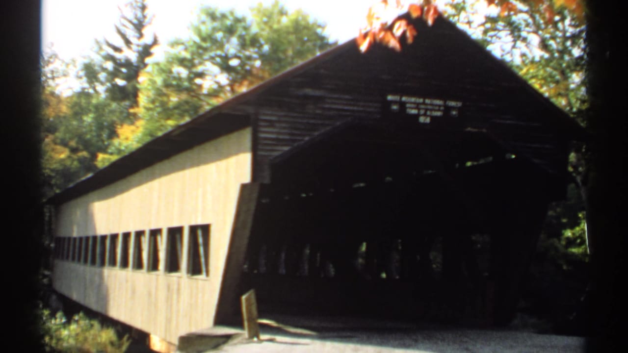 Covered bridge viewed from the front corner, with pale siding and shaded entrance.