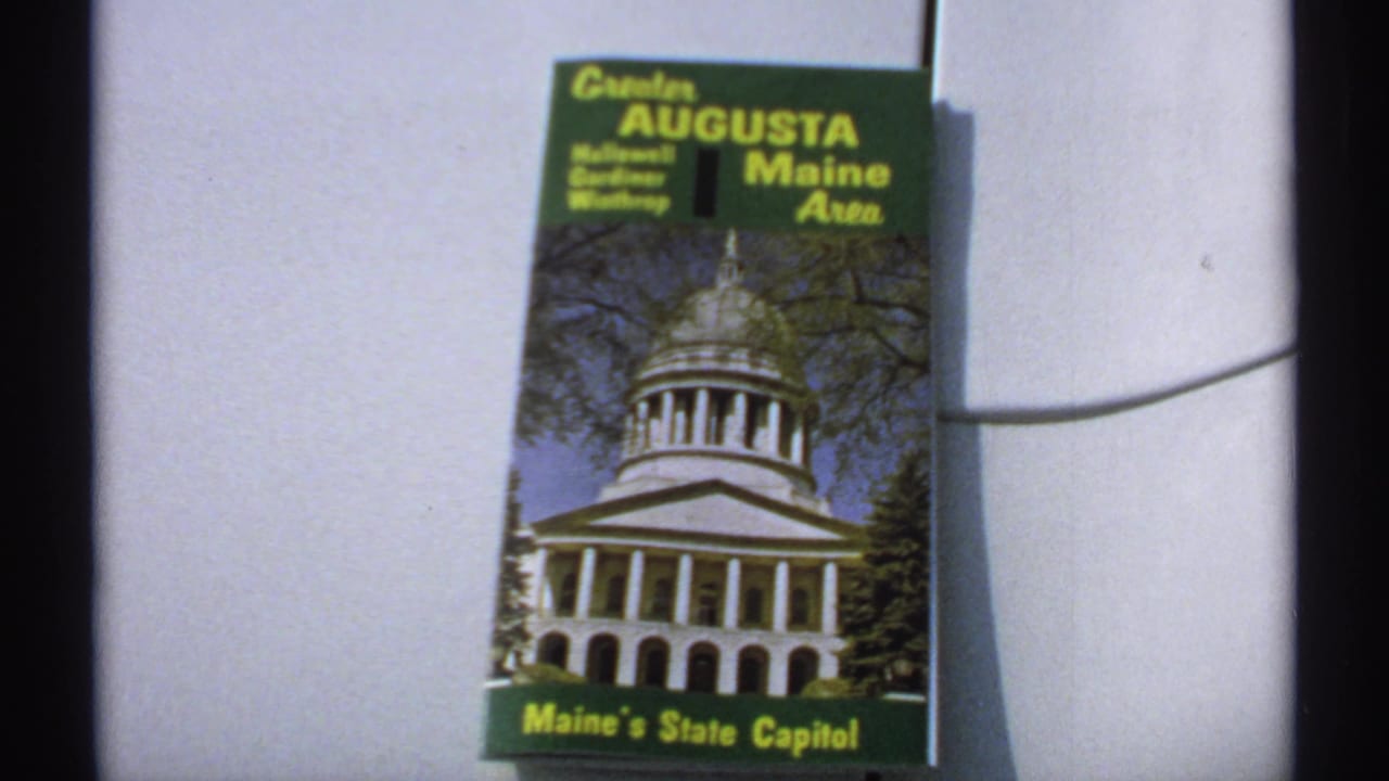 1971 8mm frame showing a Greater Augusta Maine Area travel brochure featuring Maine's State Capitol on its cover.
