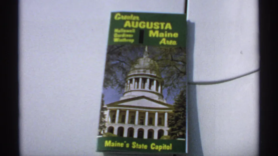 1971 8mm frame showing a Greater Augusta Maine Area travel brochure featuring Maine's State Capitol on its cover.