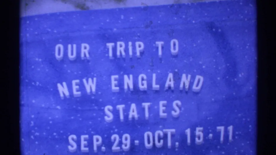 Soft 8mm frame of a blue travel title card for a New England states trip, with white lettering and visible film wear.