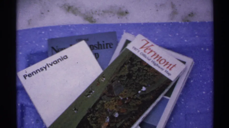 State maps for Pennsylvania, Vermont, New Hampshire, and Maine are stacked on a blue surface in 1971 8mm footage.