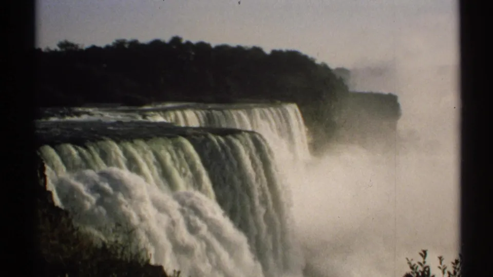 8mm home-movie frame from New York showing a broad waterfall, dark wooded rim, and heavy mist at the base.