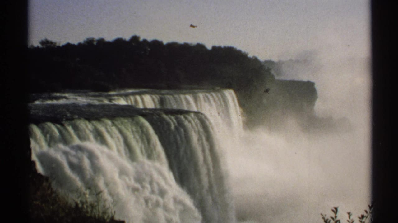 Close view of Niagara Falls with mist, treeline, and film gate edges.