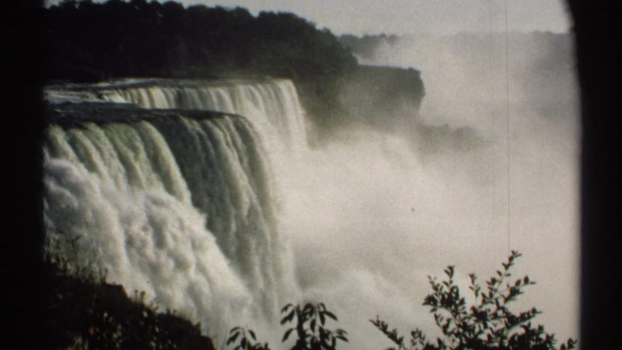 Niagara Falls seen close up with heavy mist and dark trees above the falls.