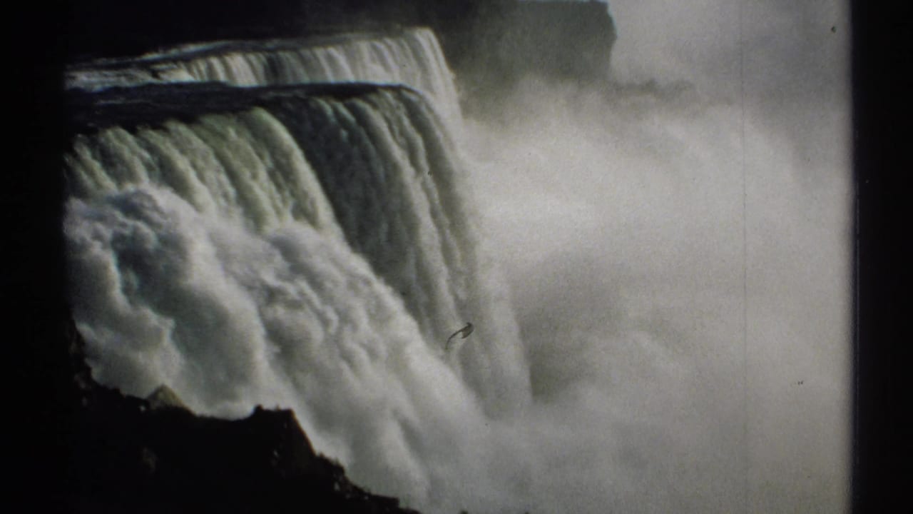 Water drops over Niagara Falls into thick mist beside a dark cliff edge.