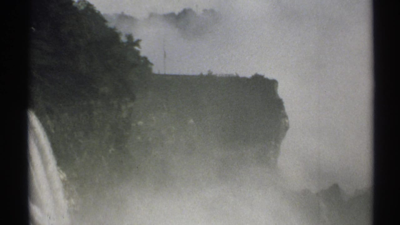 1971 New York 8mm frame showing a misty waterfall falling beside a dark tree-covered cliff, with heavy spray softening the view.